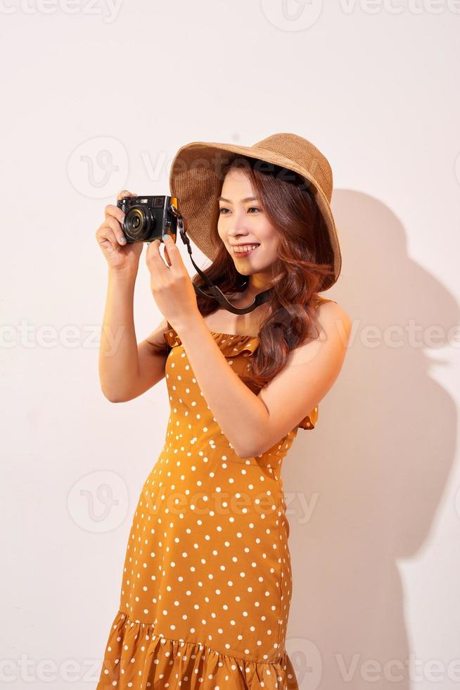 Attractive young woman with a photo camera in her hand on an isolated beige background. The concept travel