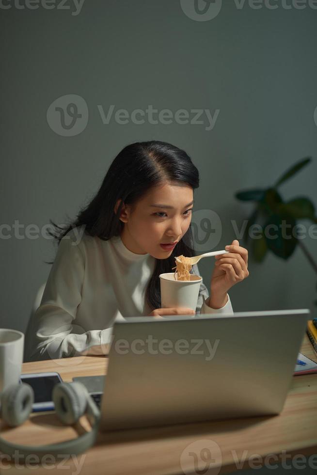 instant noodles being pulled out of disposable cup with fork and young asian woman blows on it photo