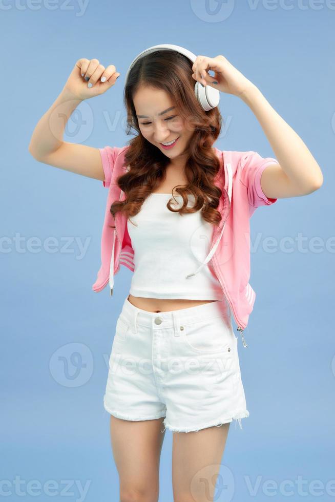 Amazing charming summer young woman in jeans shorts over colorful blue background. Dancing, listening to music with headphones photo