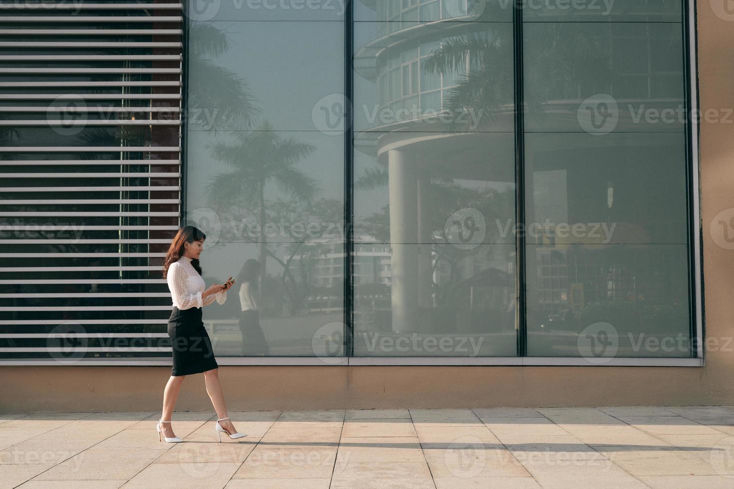Full length side portrait of a young woman walking and sending text message on cell phone photo