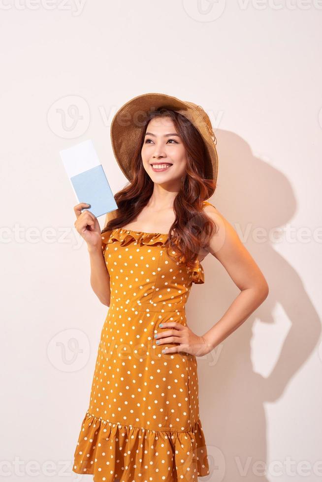 A young woman in a orange polka dots dress with a straw hat on her head is holding a passport and plane tickets photo