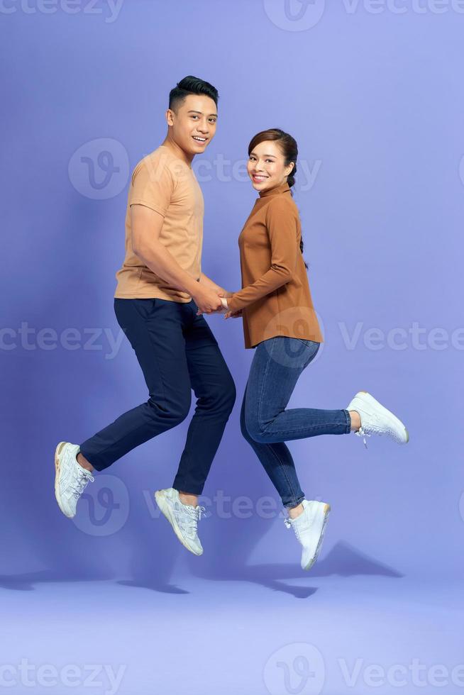 Photo of happy excited young loving couple jumping isolated over purple background.