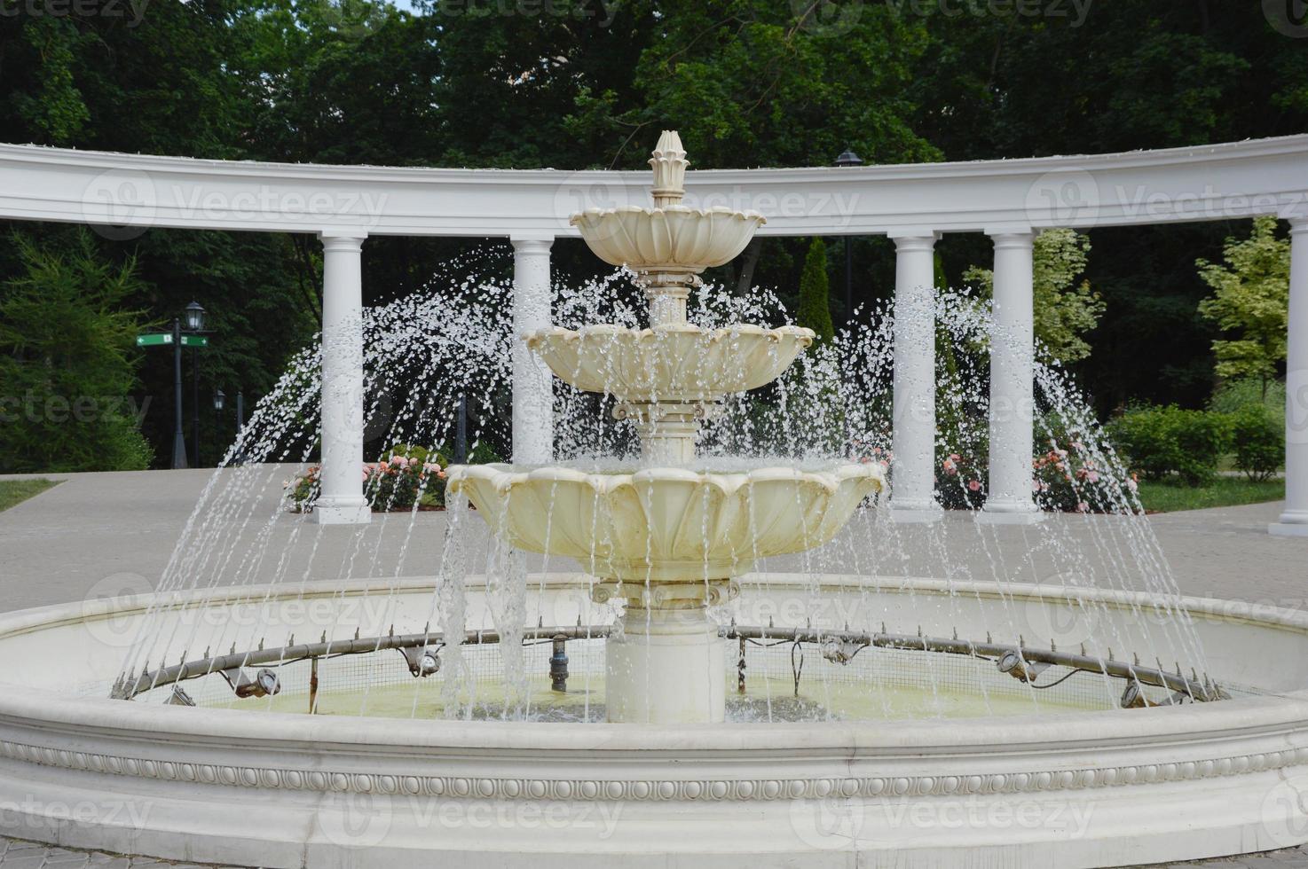 A working fountain in a city park against the backdrop of columns and green trees on a sunny summer day. photo