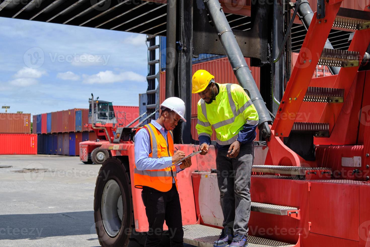 Two African American male workers in safety uniforms and hardhats use walkie-talkie, work at logistic terminal with stacks of containers, loading control shipping goods, and cargo transport industry. photo