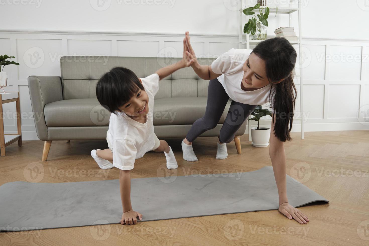 Young Asian Thai mother lovely trains her little son to exercise and practices yoga on living room floor together for healthy fitness and wellness, happy domestic home lifestyle on family weekends. photo