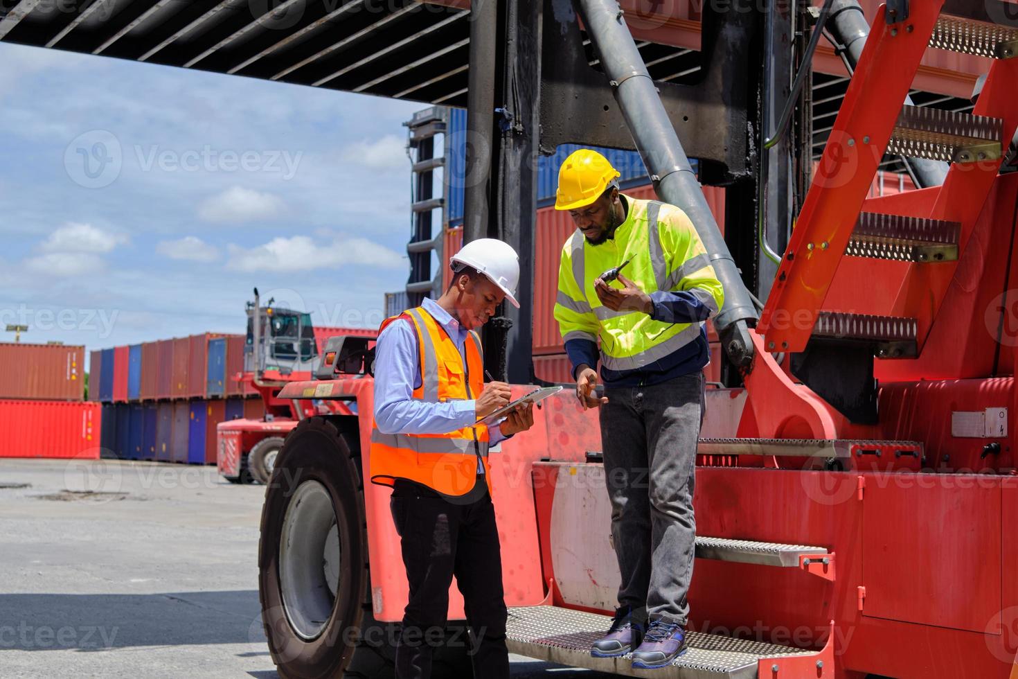 Two African American male workers in safety uniforms and hardhats use walkie-talkie, work at logistic terminal with stacks of containers, loading control shipping goods, and cargo transport industry. photo