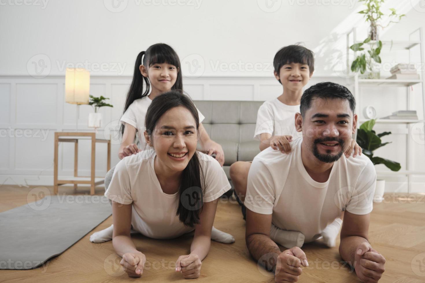 Happy well-being Asian Thai family, children play and tease their parents while yoga fitness training and health exercise together in the white living room, domestic home lifestyle, weekend activity. photo