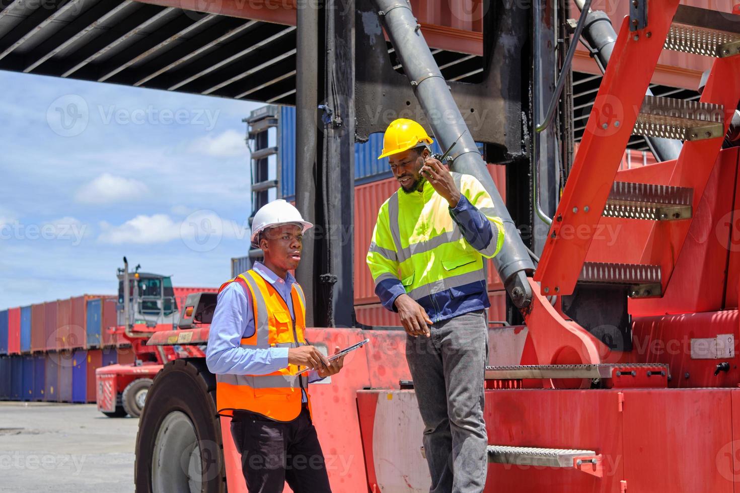 Two African American male workers in safety uniforms and hardhats use walkie-talkie, work at logistic terminal with stacks of containers, loading control shipping goods, and cargo transport industry. photo