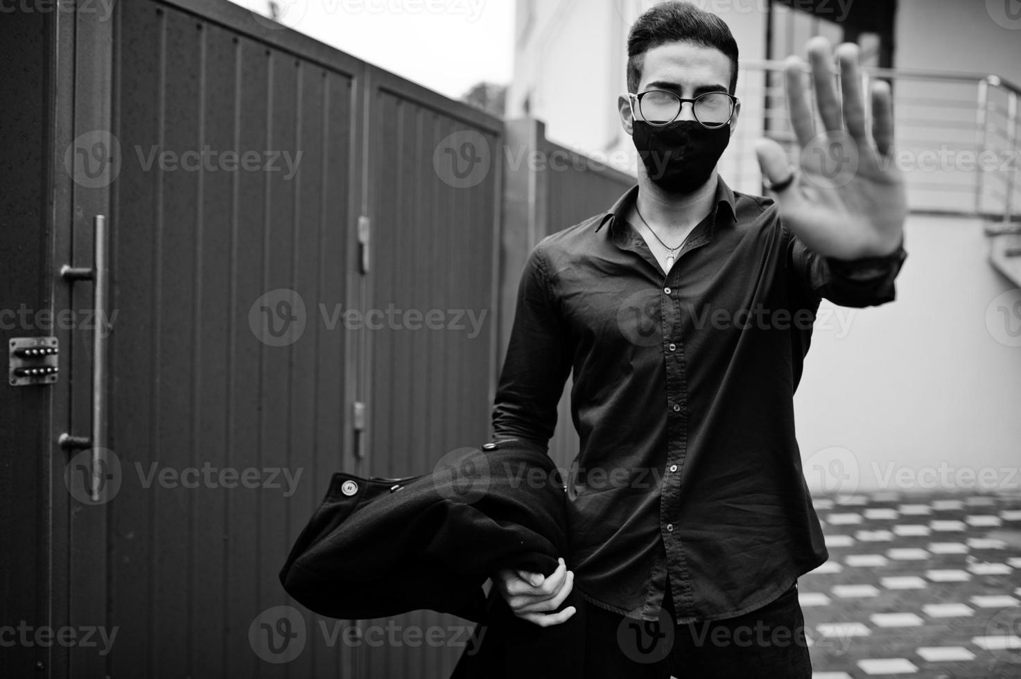 Middle eastern entrepreneur wear black face mask and eyeglasses show stop sign by hand. New normal life after coronavirus pandemia. photo