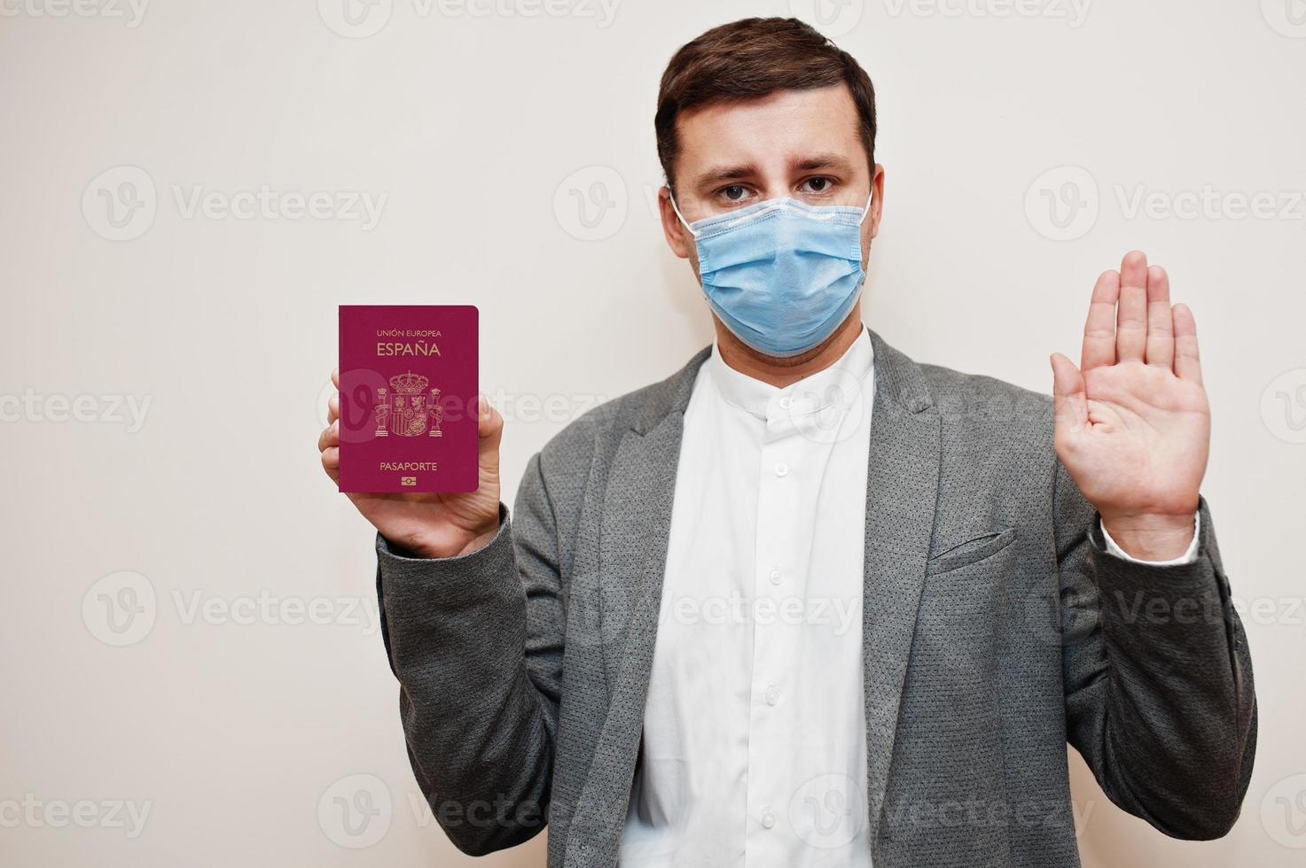 European man in formal wear and face mask, show Spain passport with stop sign hand. Coronavirus lockdown in Europe country concept. photo