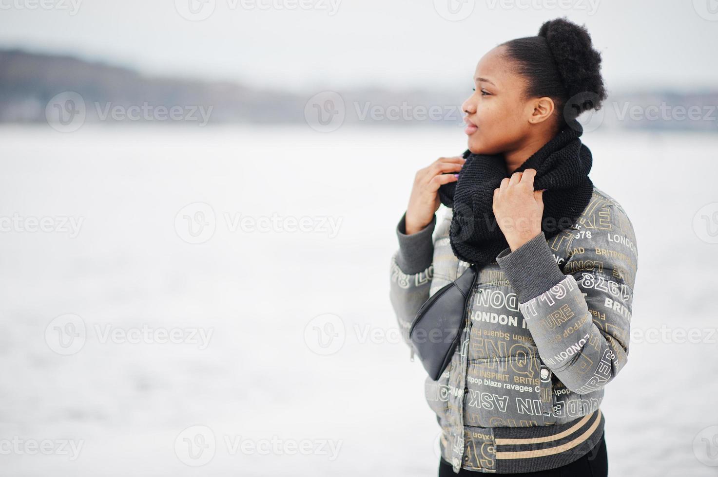 mujer africana vestida con bufanda negra posada en un lago de hielo congelado, día de invierno en europa. foto