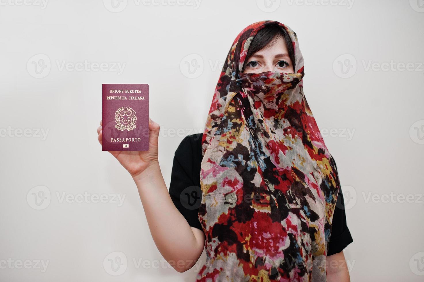 una joven musulmana árabe vestida con hiyab tiene pasaporte de la república italiana con fondo de pared blanca, retrato de estudio. foto