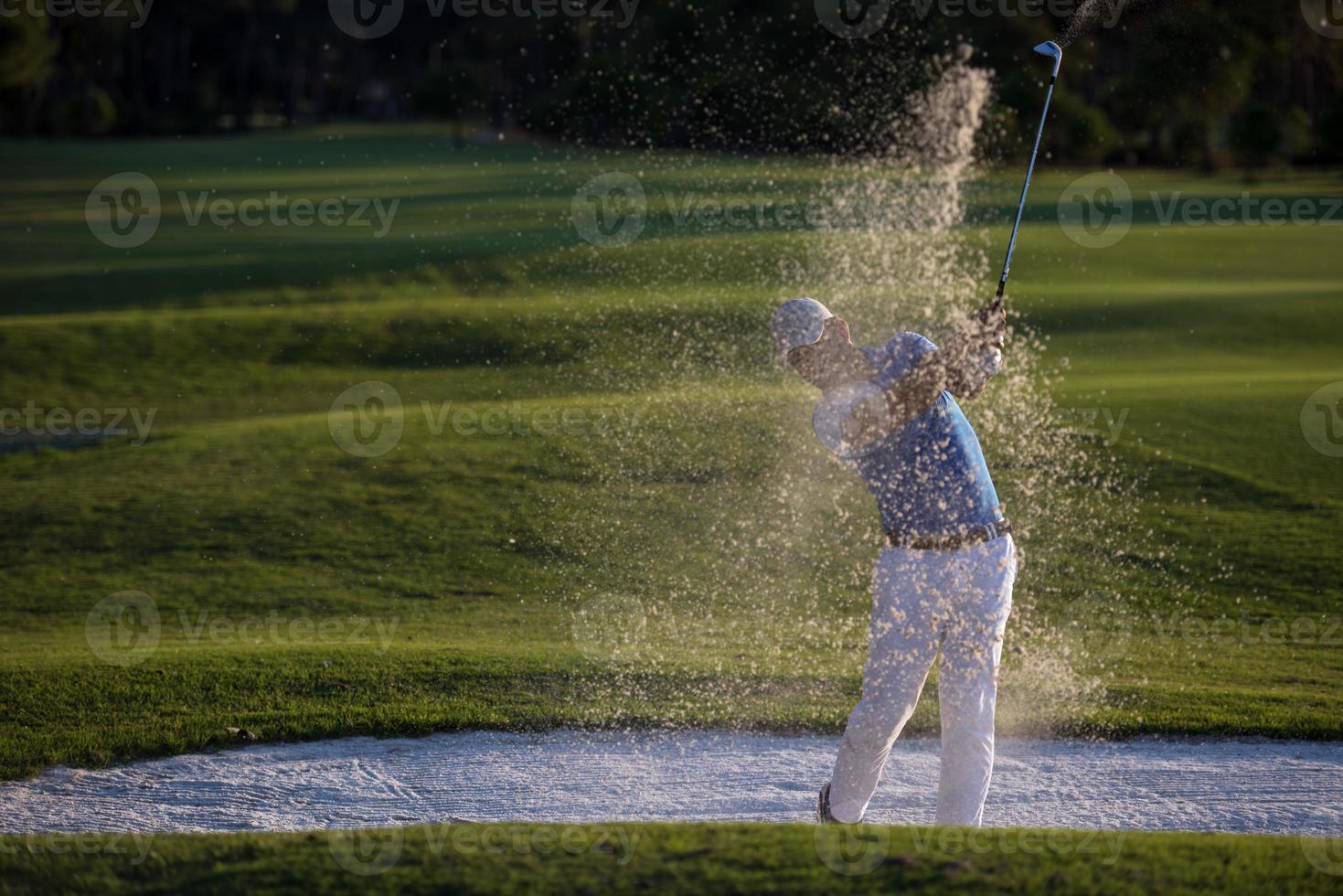 golfer hitting a sand bunker shot on sunset photo