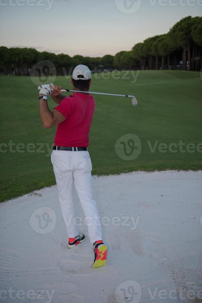 golfer hitting a sand bunker shot on sunset photo