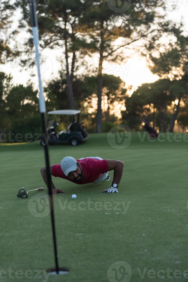 golf player blowing ball in hole with sunset in background photo