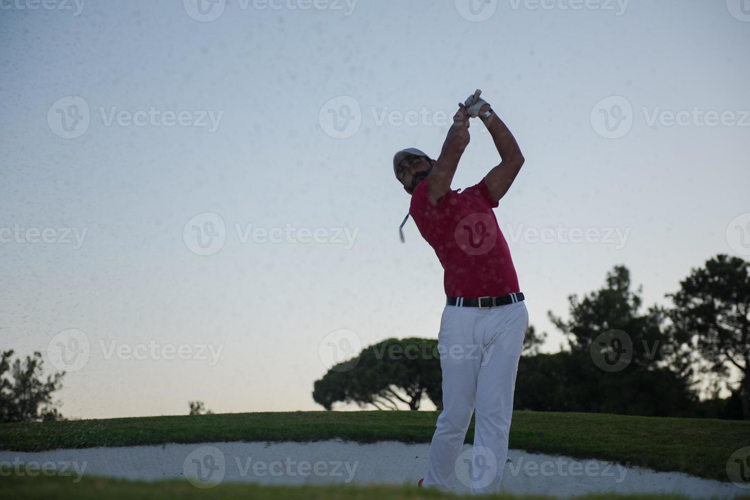 golfer hitting a sand bunker shot on sunset photo