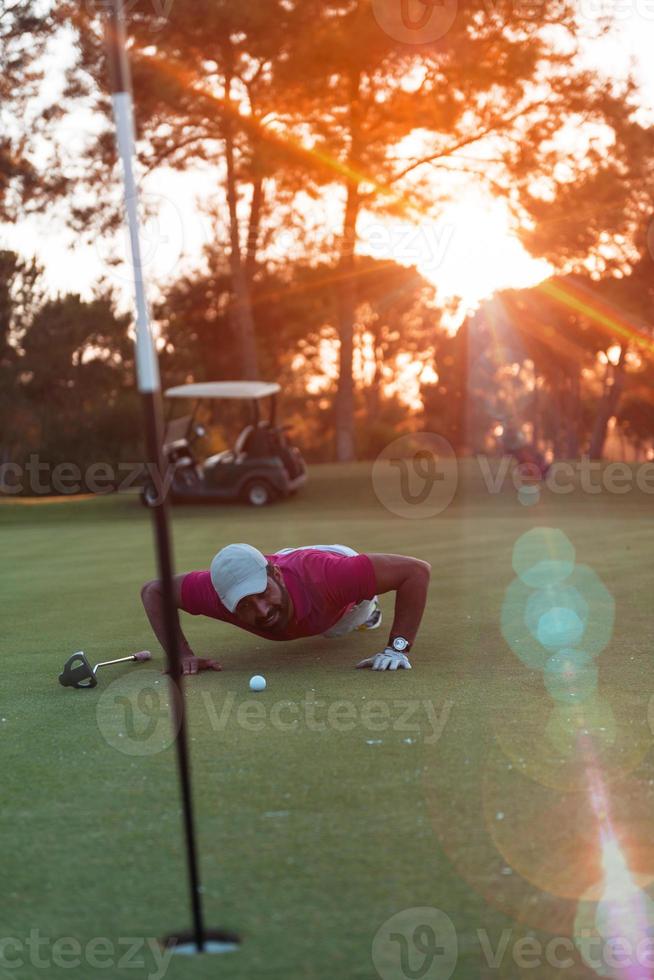 golf player blowing ball in hole with sunset in background photo