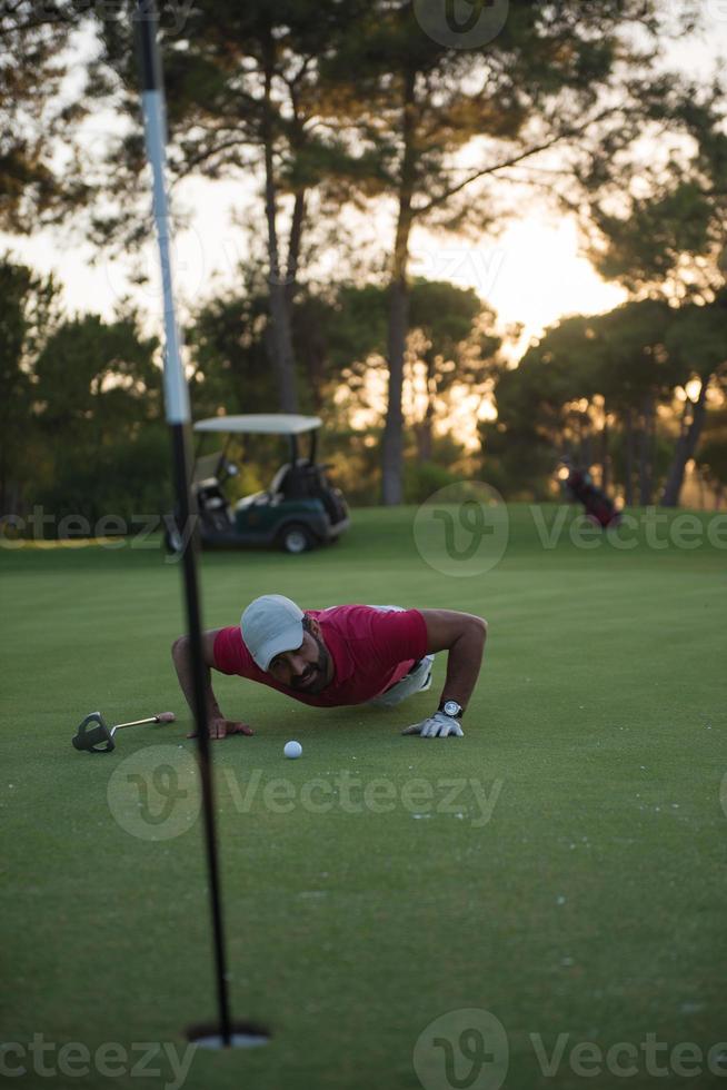 golf player blowing ball in hole with sunset in background photo