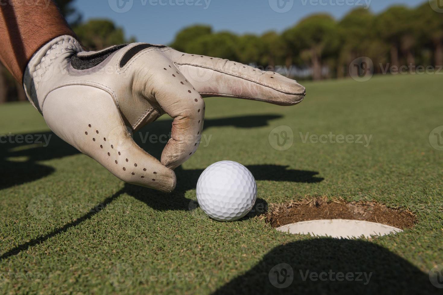 man's hand putting golf ball in hole photo