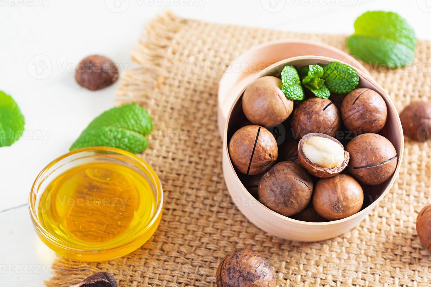Macadamia nuts in shell with mint leaves and honey on wooden background photo