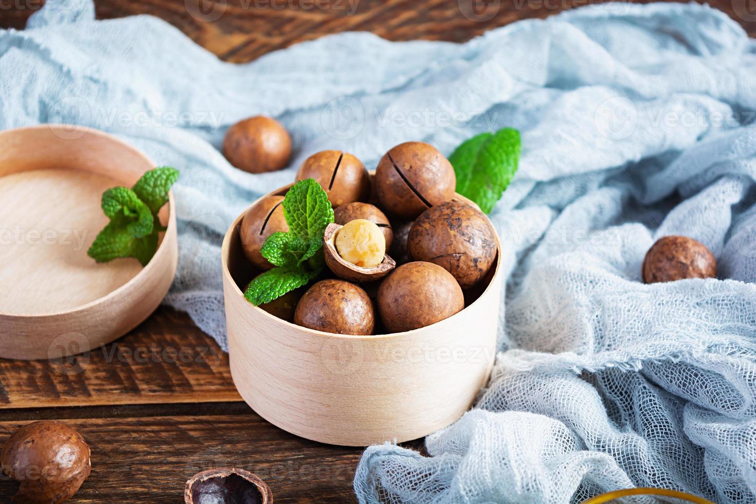 nueces de macadamia con cáscara con hojas de menta y miel sobre fondo de madera foto