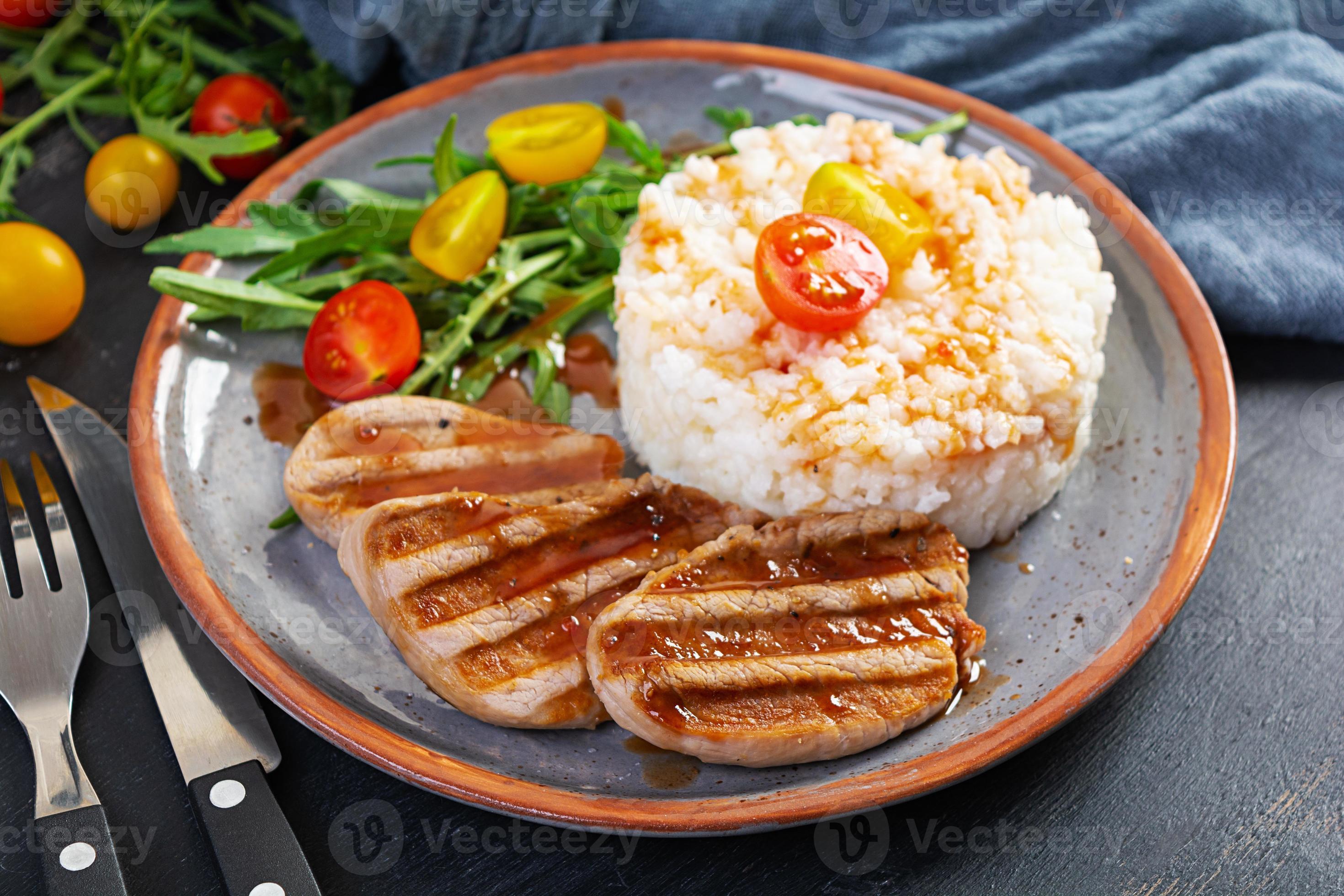 Rice with grilled pork meat, tomatoes and green herbs on dark