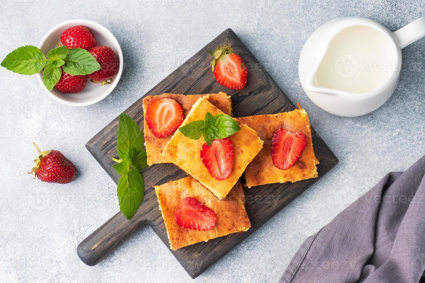 Cottage cheese casserole with strawberries and mint. Delicious homemade dessert made of curd and fresh berries with cream. Gray concrete background close up. photo