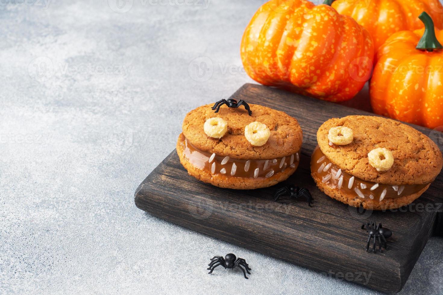 Cookies with cream paste in the shape of monsters for Halloween celebration. Funny homemade faces made of oatmeal cookies and boiled condensed milk. copy space photo