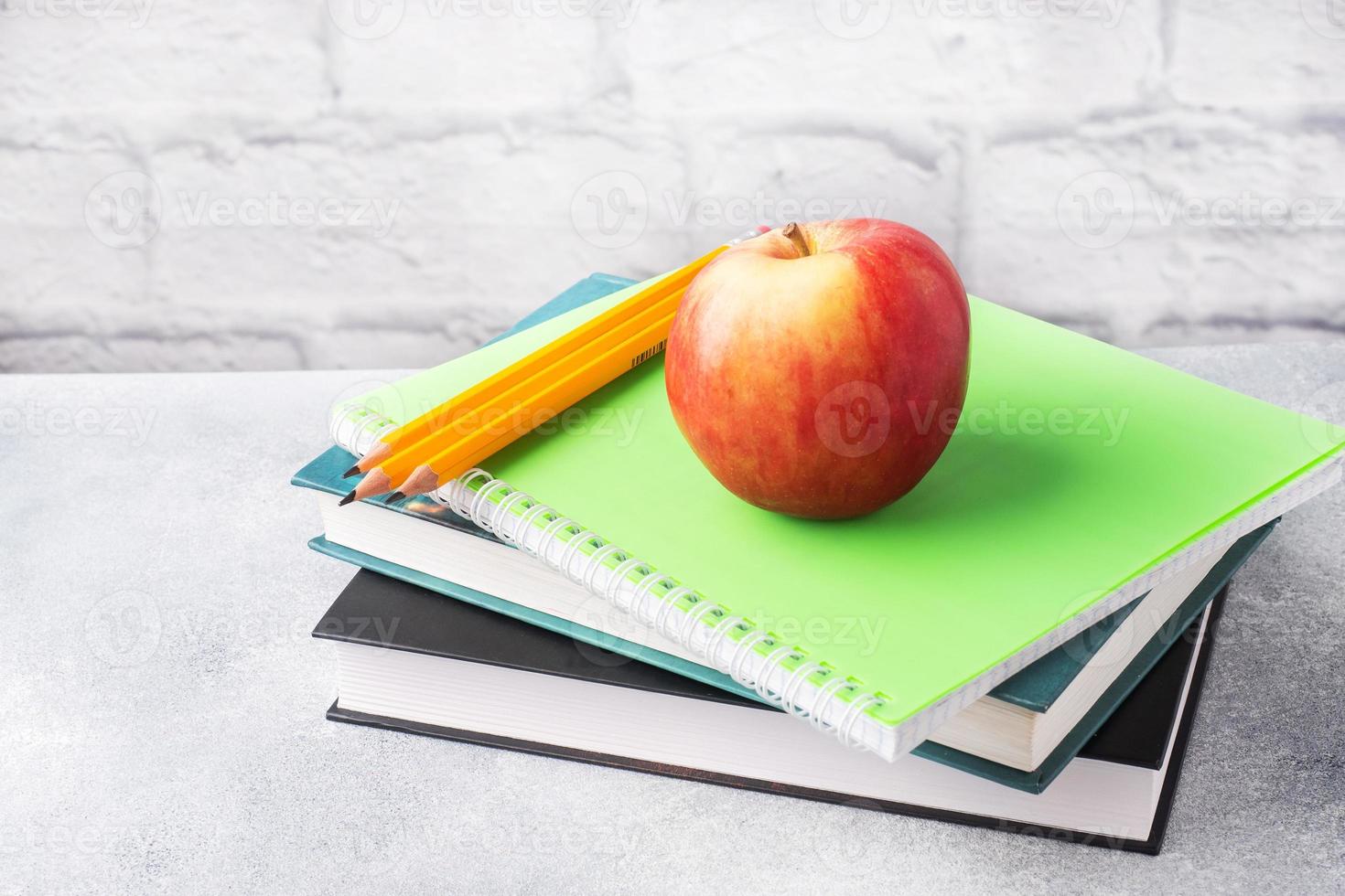A fresh red apple on a stack of books and notebooks. The concept of a school breakfast snack. Copy space, photo