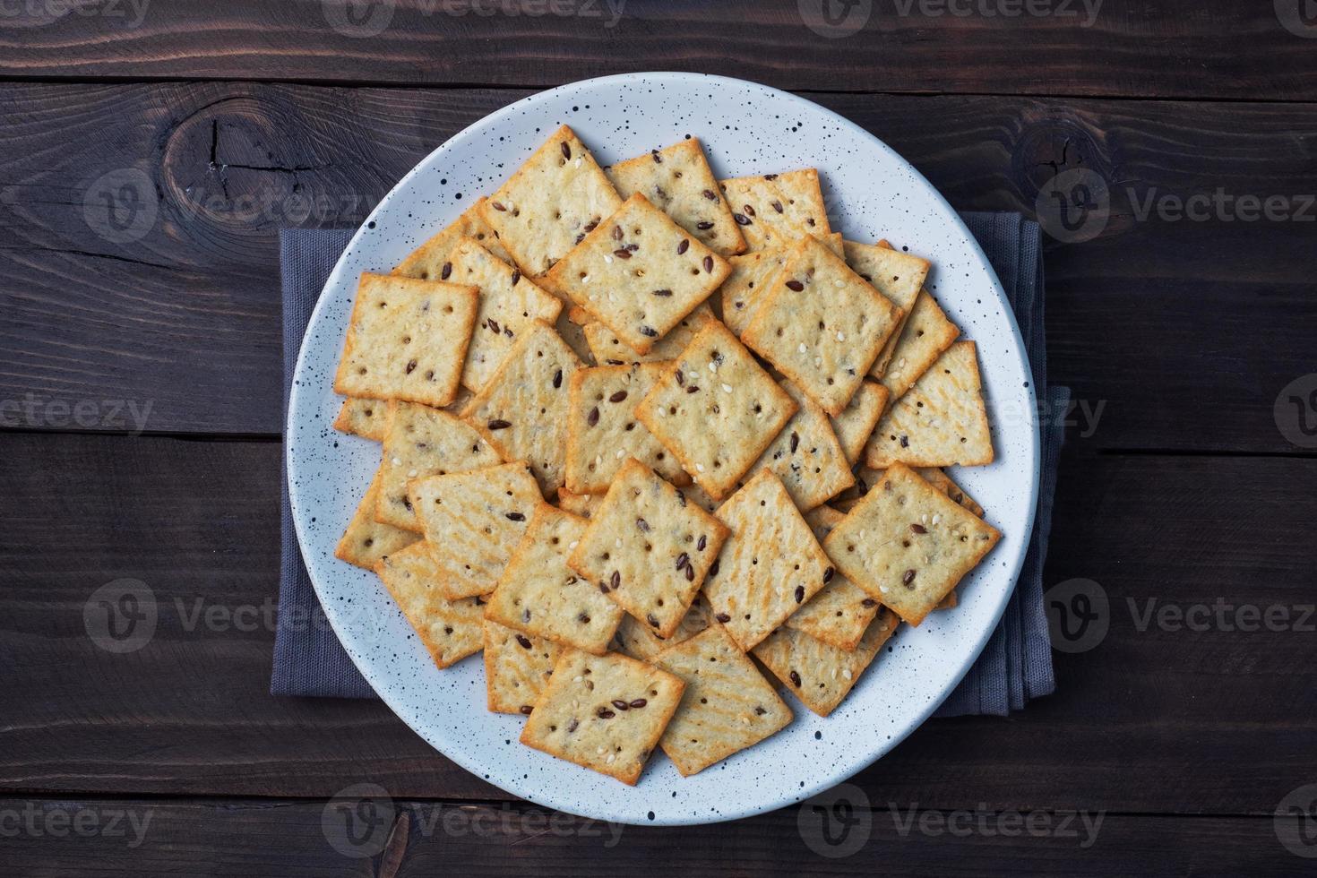 Delicious healthy cookies crackers with flax seeds and sesame seeds on a plate. Background of a healthy snack food, dark rustic wooden table. Copy space. photo