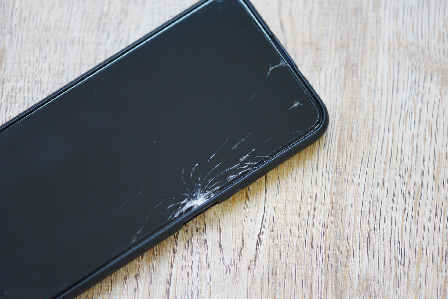 Smartphone broken glass screen on wood background - mobile phone broken screen wait change film screen in the repair shop concept photo