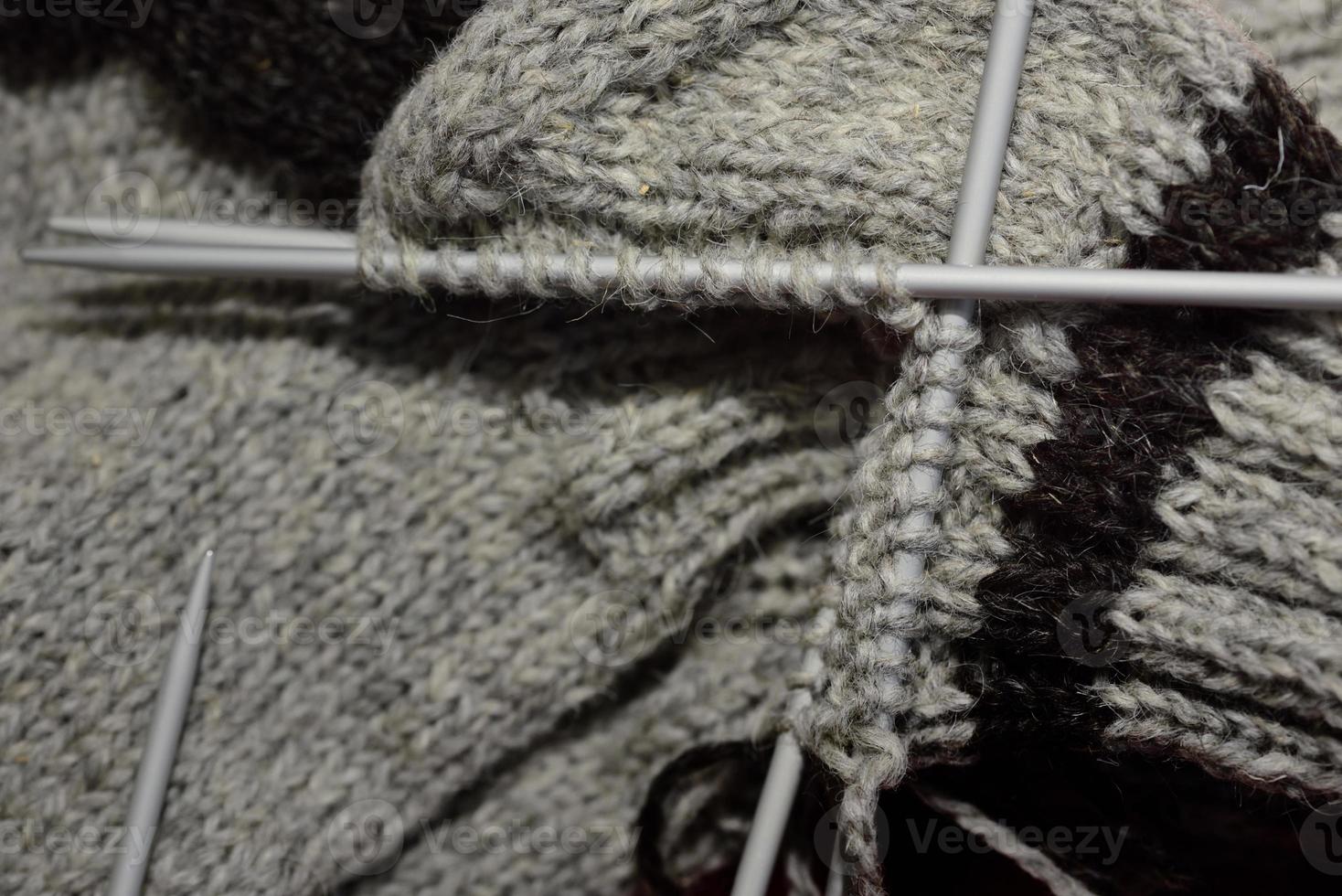 Close-up of a half-finished knitted gray woolen coarse sock with knitting needles, which is knitted by hand. photo