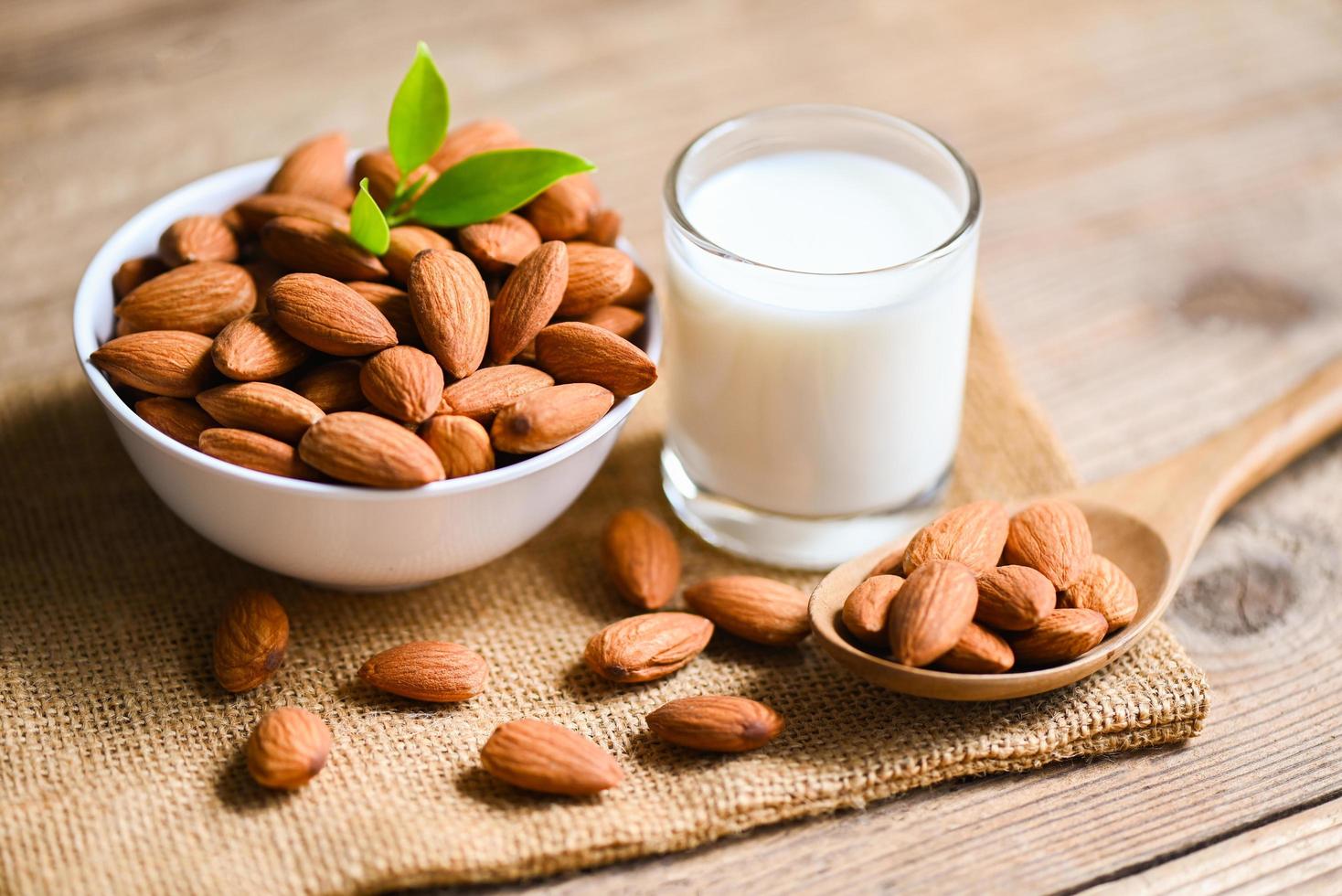 Almond milk and Almonds nuts on white bowl with green leaf on sack background, Delicious sweet almonds on the wooden table , roasted almond nut for healthy food and snack photo