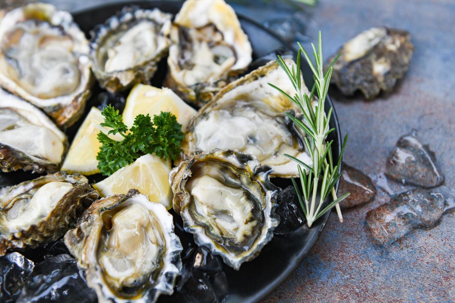 ostras frescas mariscos sobre un fondo de placa negra - concha de ostra abierta con hierbas especias limón romero servido mesa y hielo marisco saludable cena de ostras crudas en el restaurante comida gourmet foto