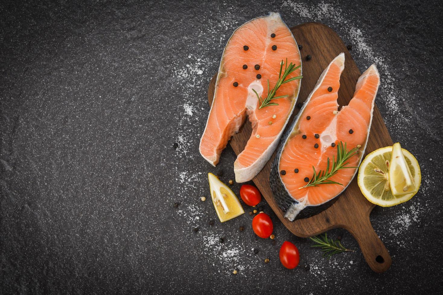 bistec de salmón fresco con hierbas y especias, limón, romero, tomate sobre fondo de madera - filete de salmón crudo y hielo para bistec cocido, marisco, vista superior foto