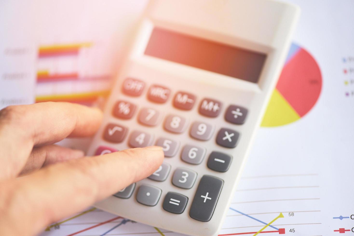 Business man using calculator for report financial statistics documents on infographics at office table close up - Sales report concept photo