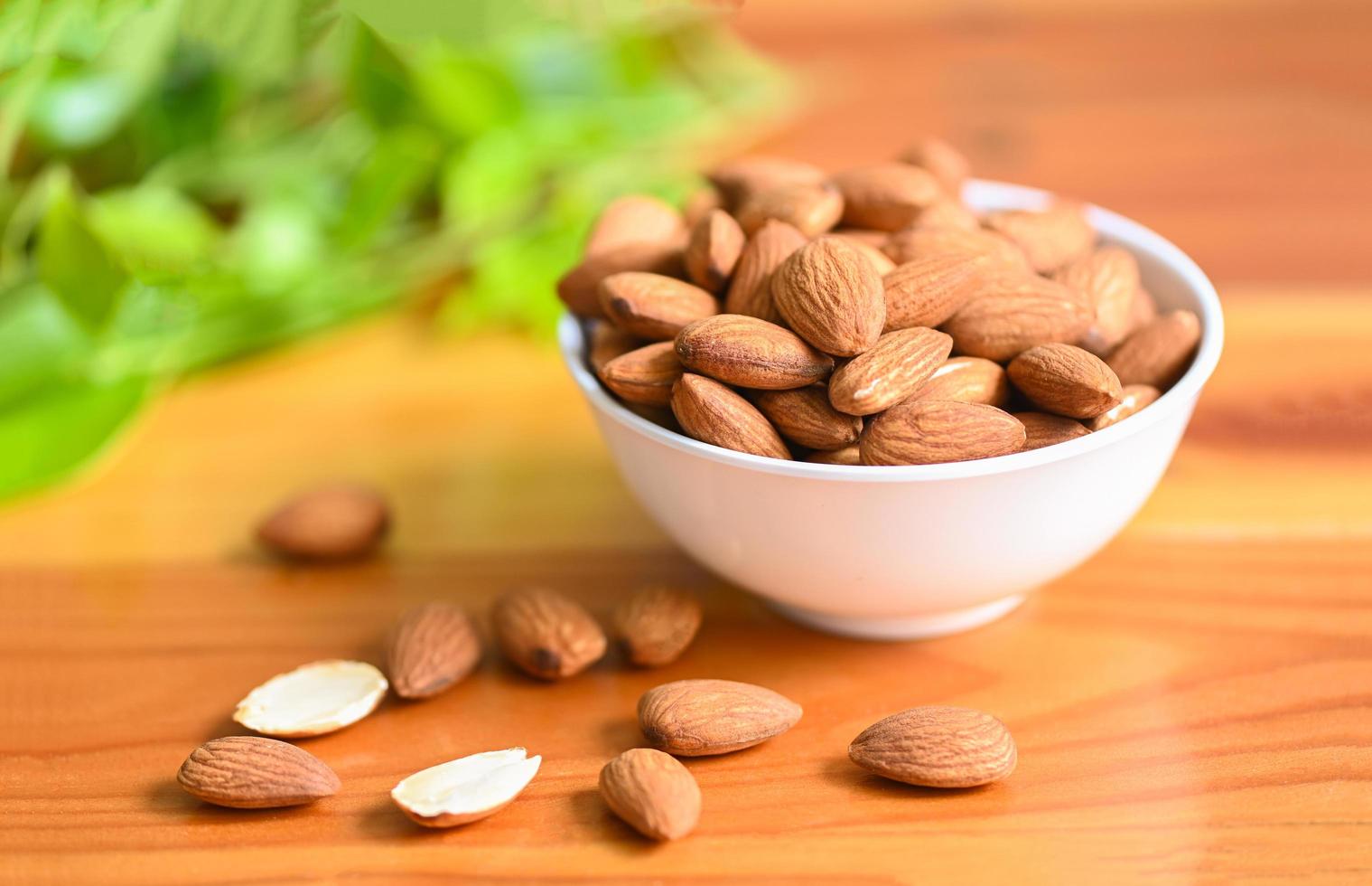 Almonds nuts on white bowl and green leaf on background, Delicious sweet almonds on the wooden table , roasted almond nut for healthy food and snack photo