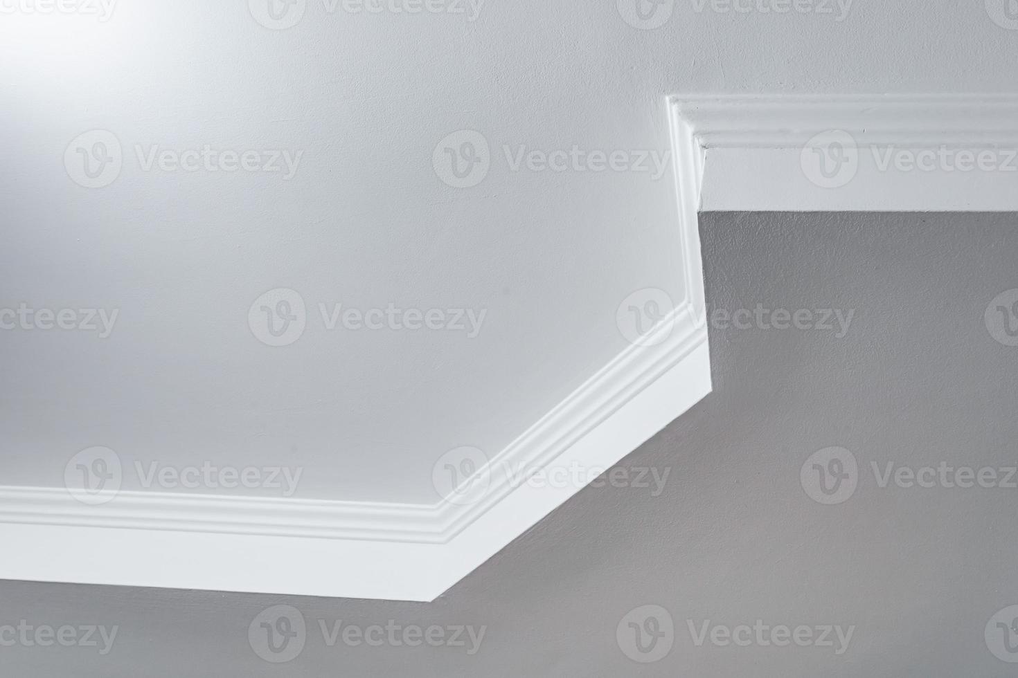 Detail of corner ceiling with intricate crown molding. Suspended ceiling and drywall construction in empty room in apartment or house. Stretch ceiling white and complex shape. photo