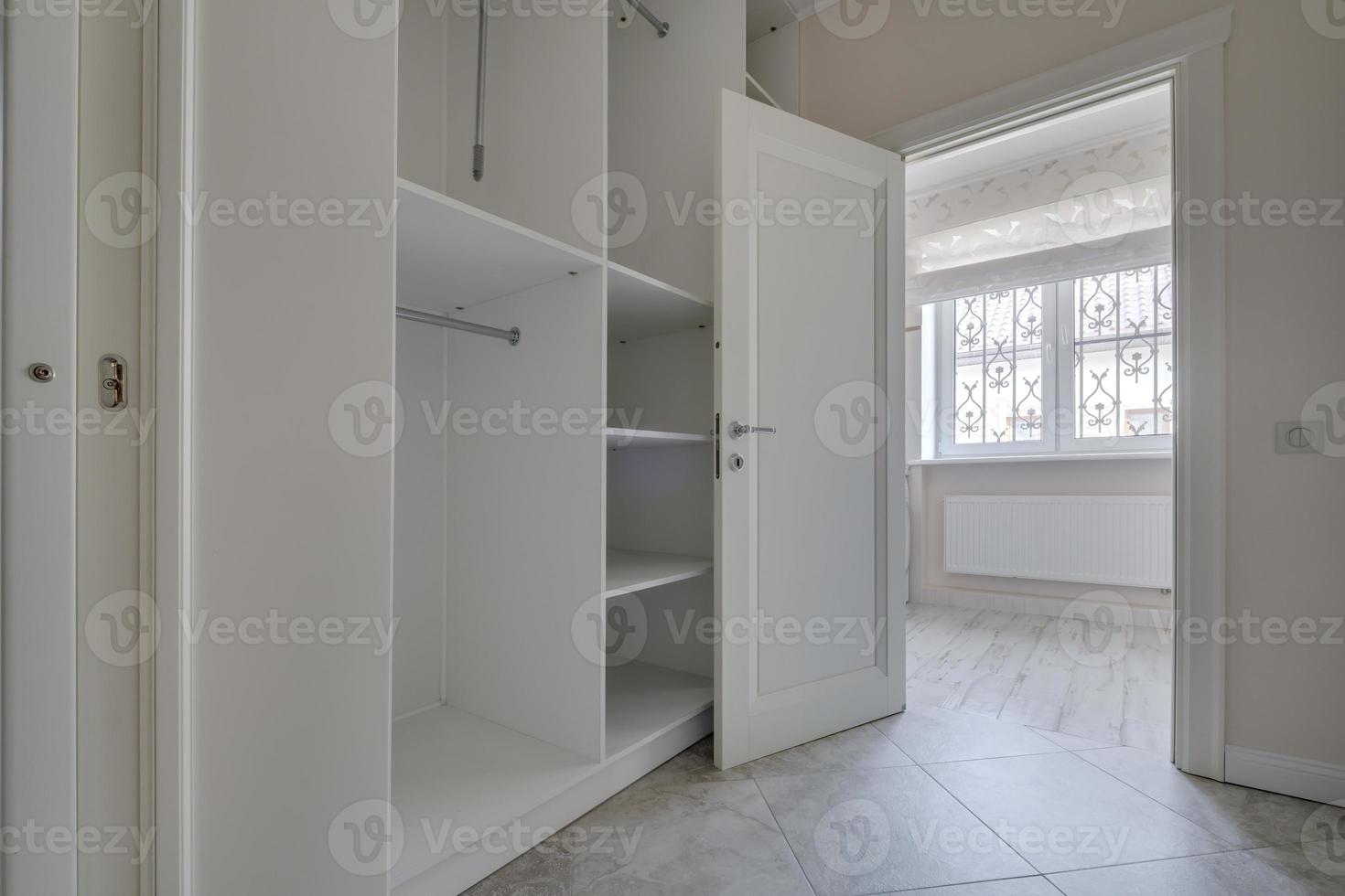 rows of shelves and clothes hangers in empty big wardrobe room in modern apartment or hotel photo