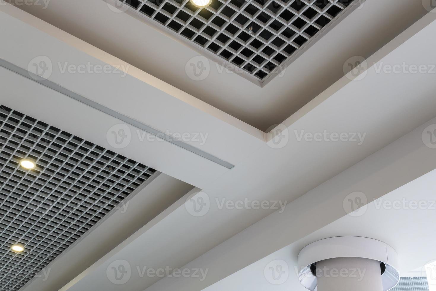 suspended and grid ceiling with halogen spots lamps and drywall construction in empty room in store or house. Stretch ceiling white and complex shape. photo