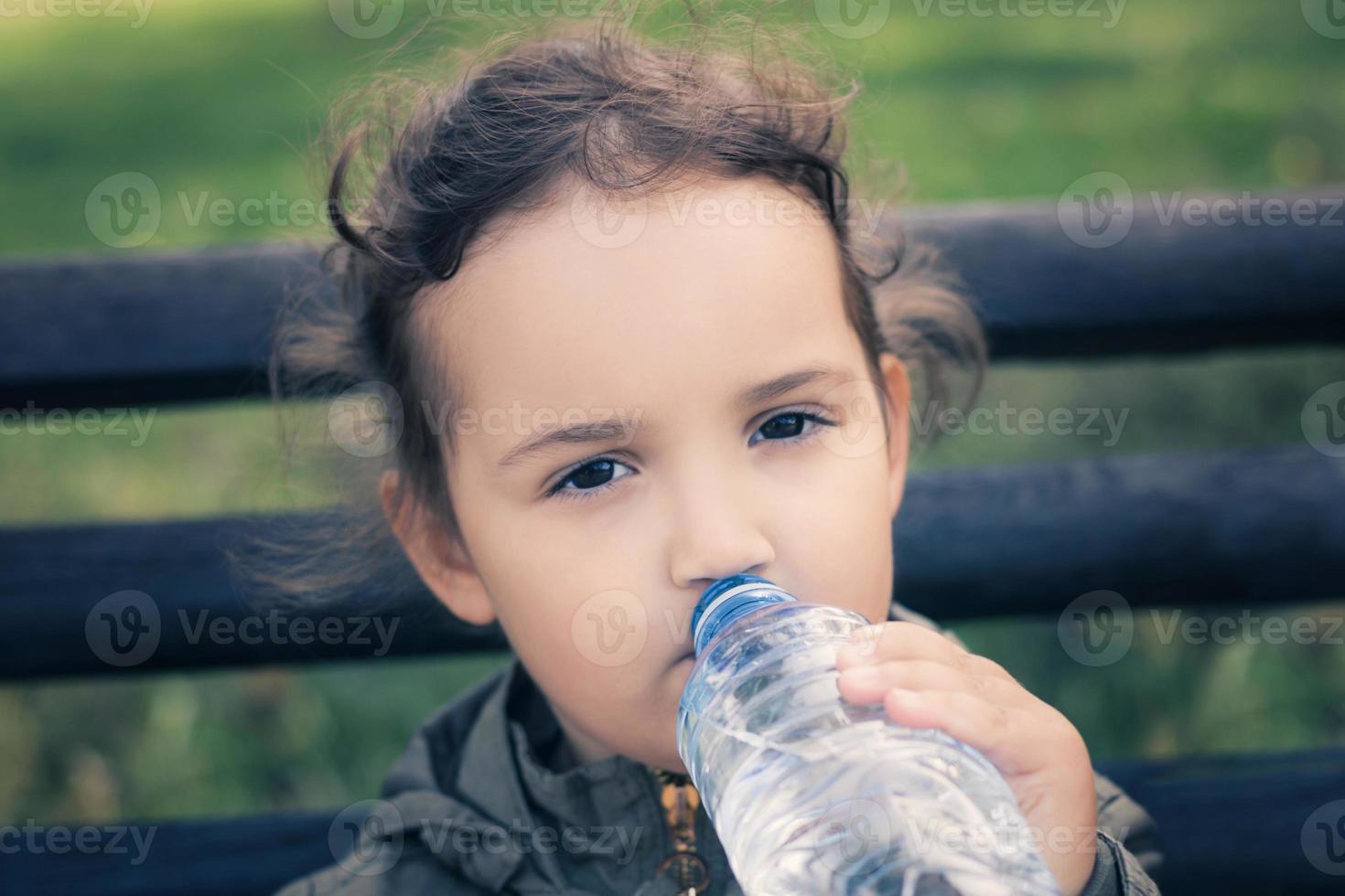 Little girl drinking water from plastic bottle. photo