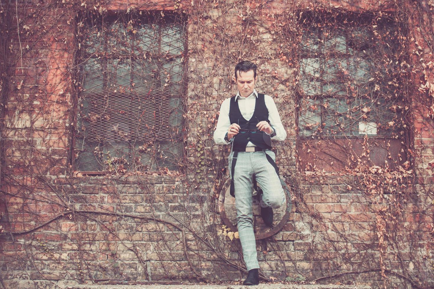 Full length of man holding sunglasses while leaning on a wall. photo