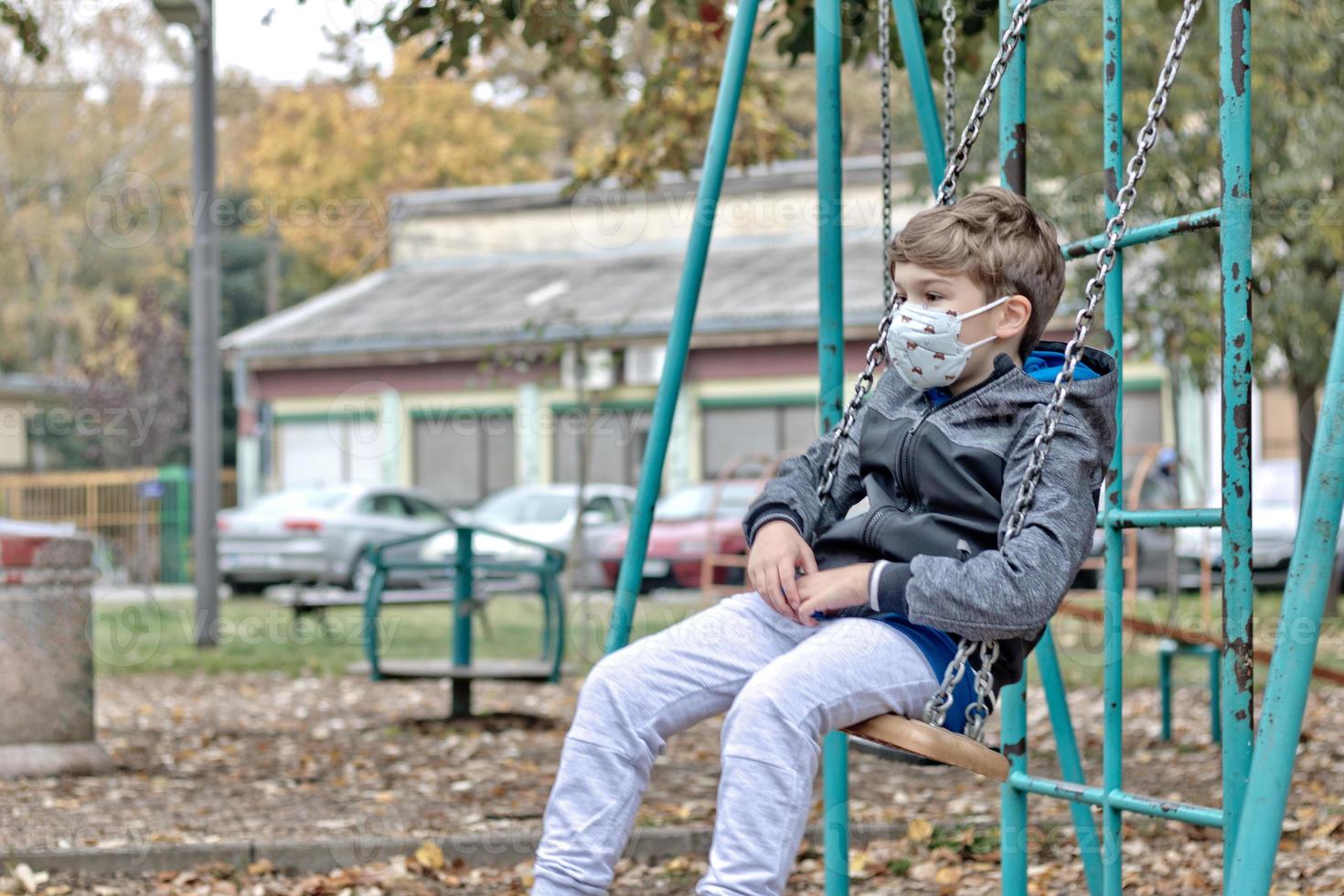 Small kid with protective face mask swinging at the playground. photo