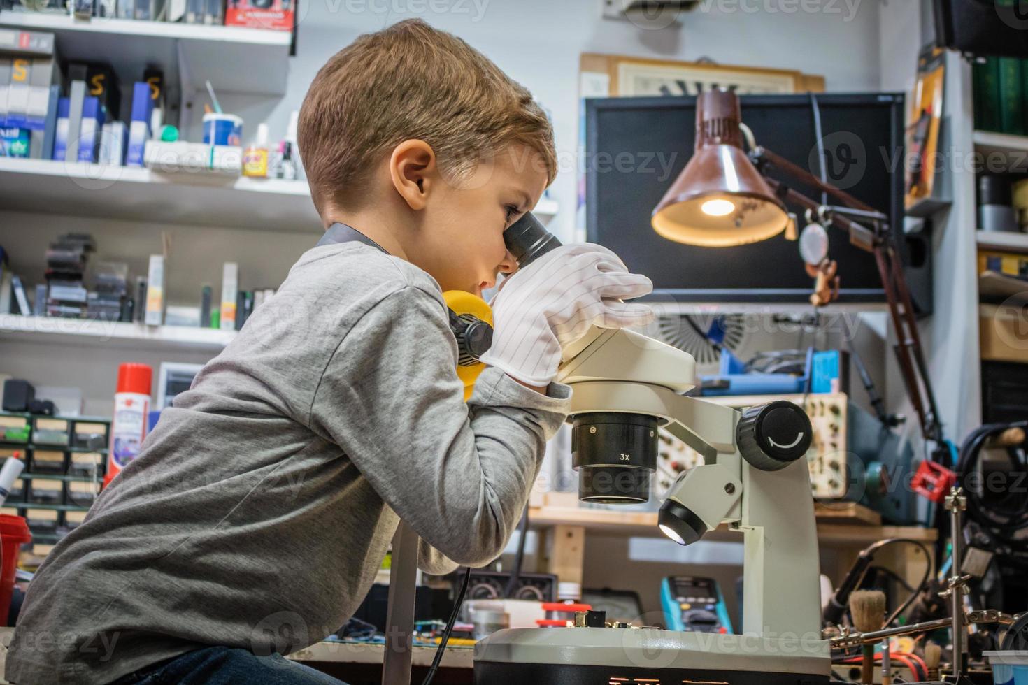 Small boy looking through microscope in tech laboratory. photo