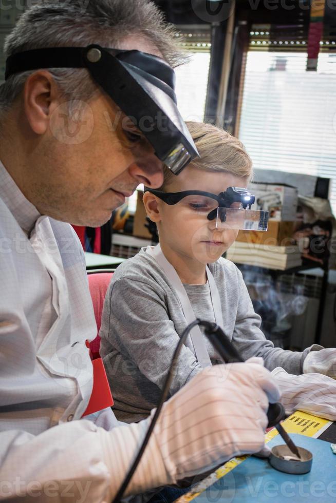 el profesor de ingeniería le está enseñando a un niño pequeño cómo usar el soldador. foto