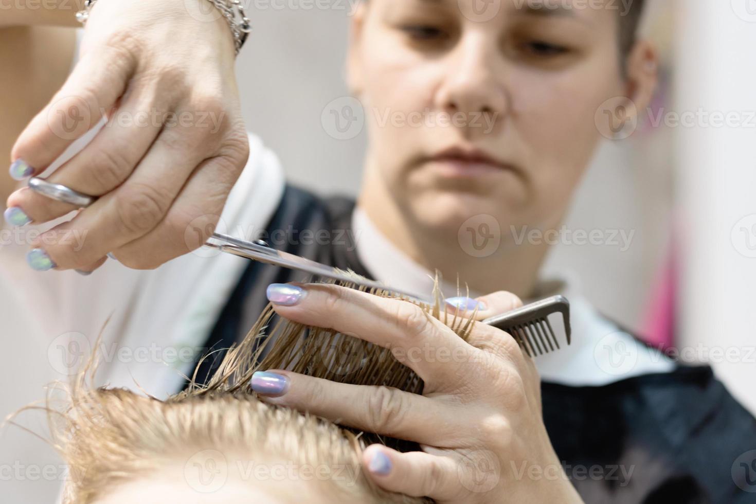 Close up of hairdresser cutting boy's hair with scissors. photo