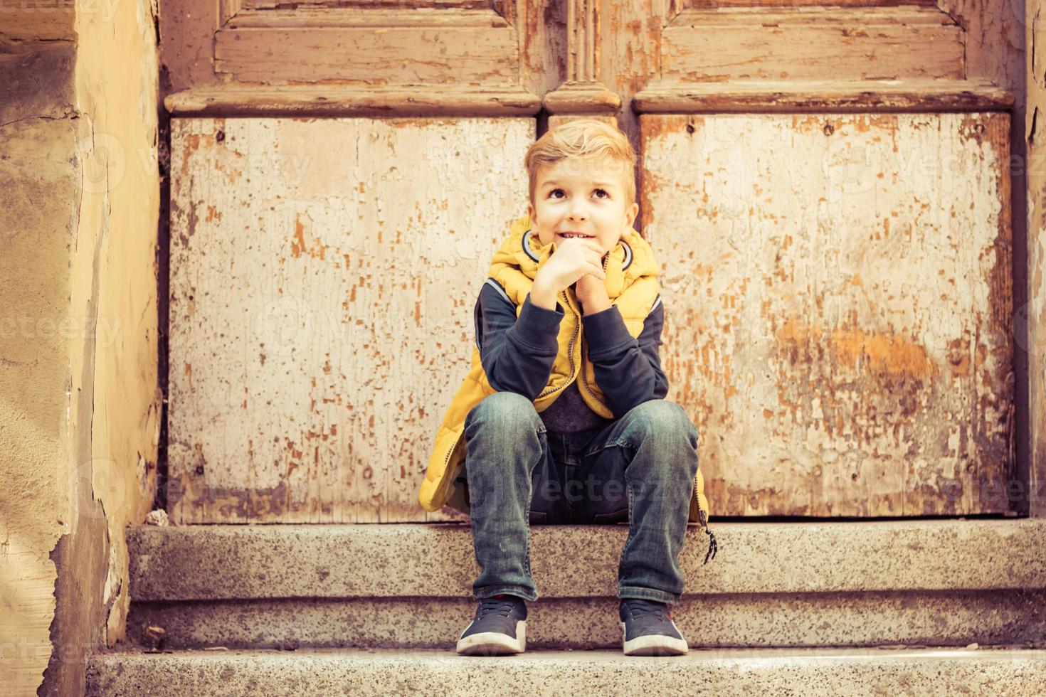 Cute kid sitting on steps and thinking of something. photo