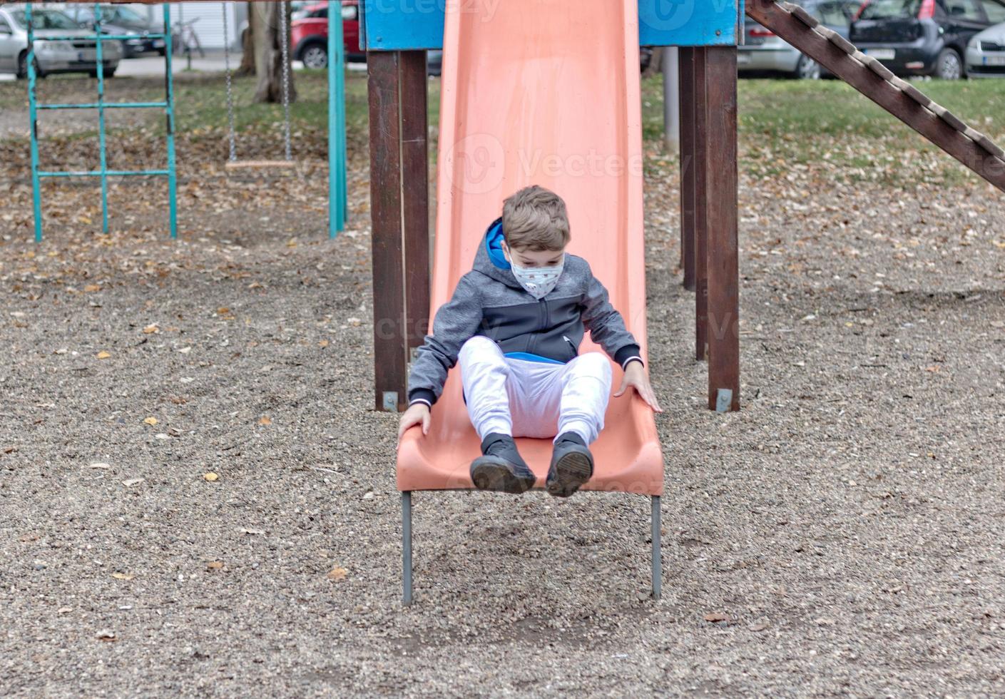 Playful kid with face mask having on a slide at the playground. photo