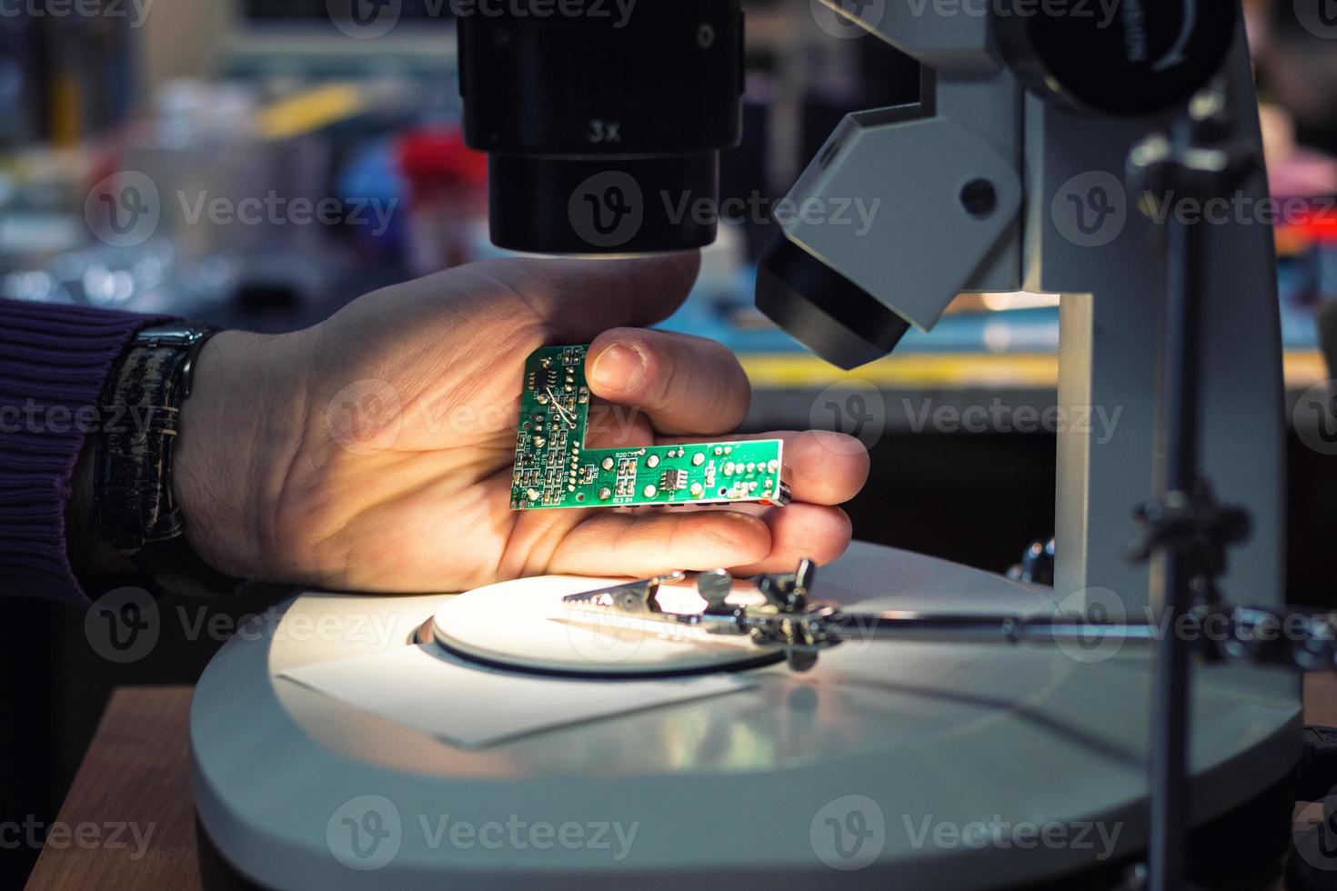 Close up of IT technician examining computer part under microscope photo