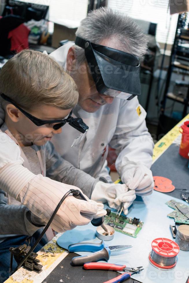 Science teacher and small boy soldering mother board in a laboratory. photo
